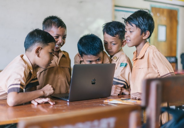 Kinder stehen in der Schule um einen Laptop